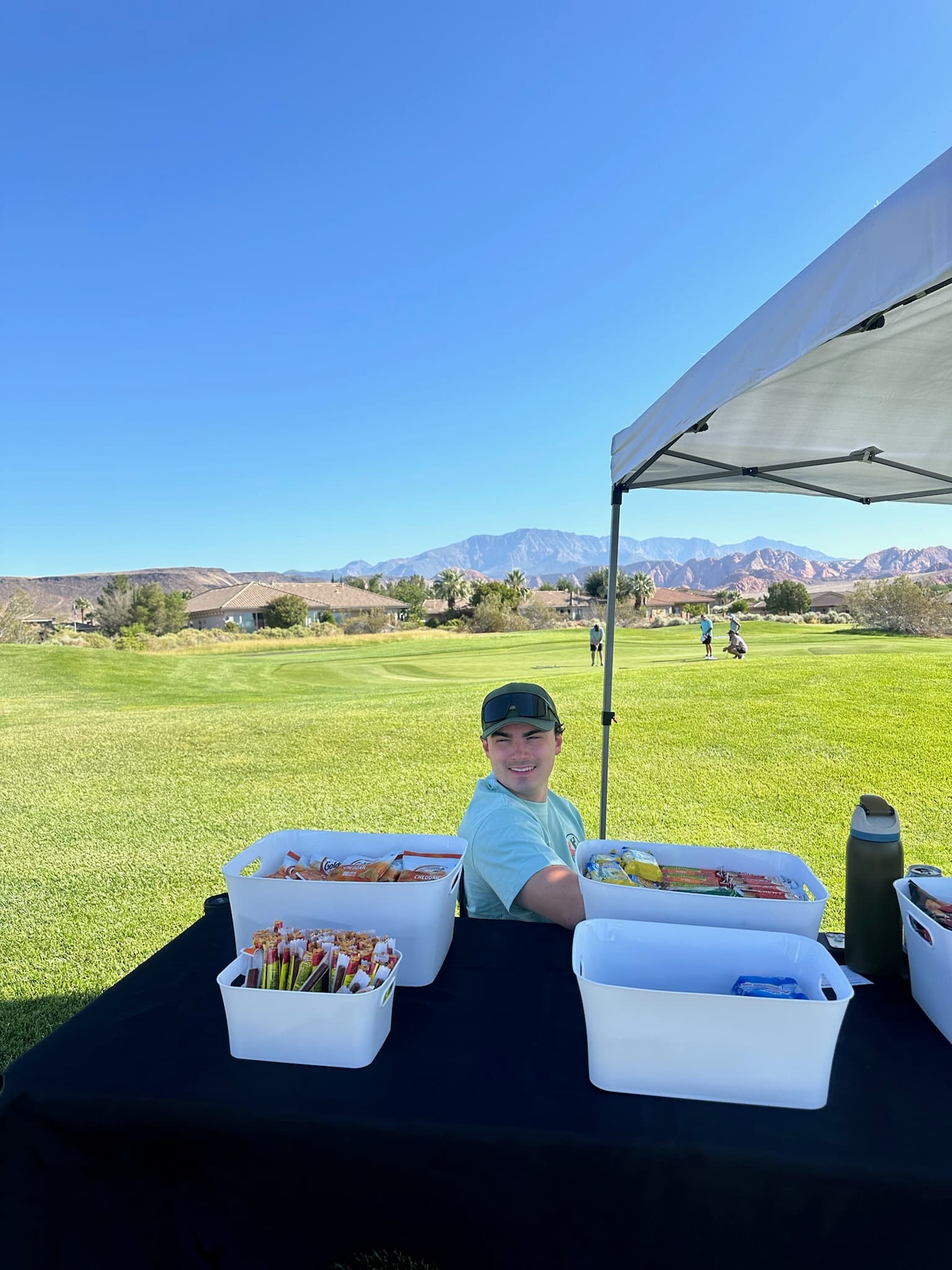 Volunteer at the snack station with a mountain fairway view during a past Clubs and Scrubs event